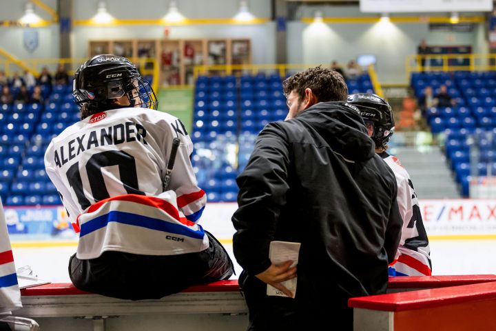 Image of player sitting on the boards and talking to a coach